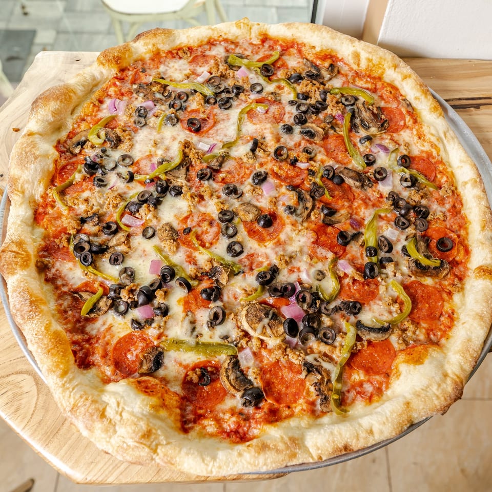 Large cheesy pizza topped with pepperoni, sausage, mushrooms, black olives, green peppers, and red onions on a wooden table.