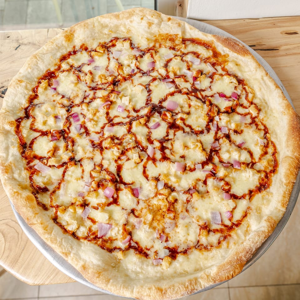 Large cheesy pizza topped with diced red onions, chicken, and barbecue sauce on a wooden table.