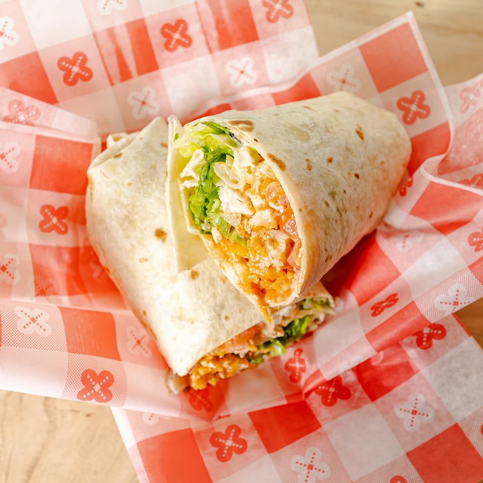 Two toasted chicken wraps filled with lettuce, tomatoes, cheese, and sauce on red-and-white patterned paper.