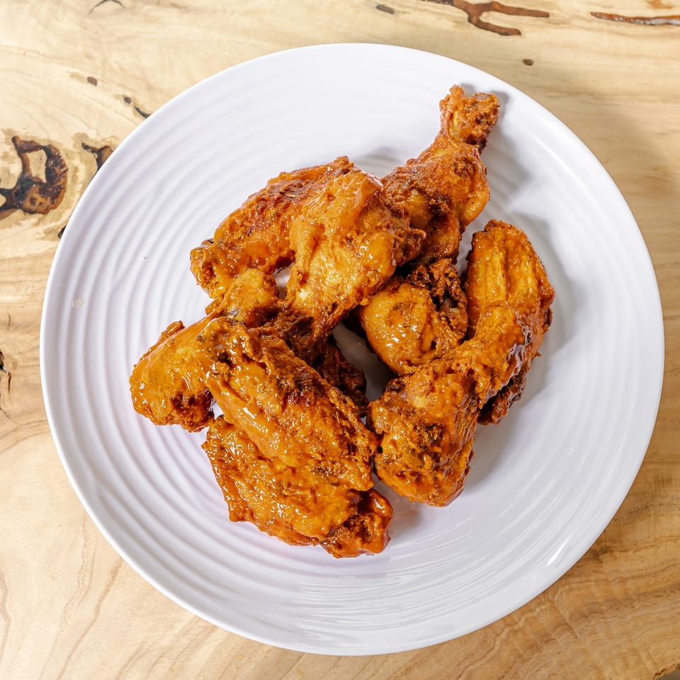 Crispy, sauce-coated fried chicken wings piled on a white plate atop a rustic wooden table.