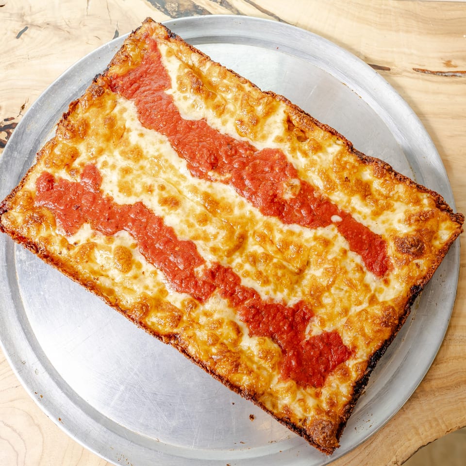 Large rectangular pizza topped with melted cheese and tomato sauce on a metal tray atop a wooden table.