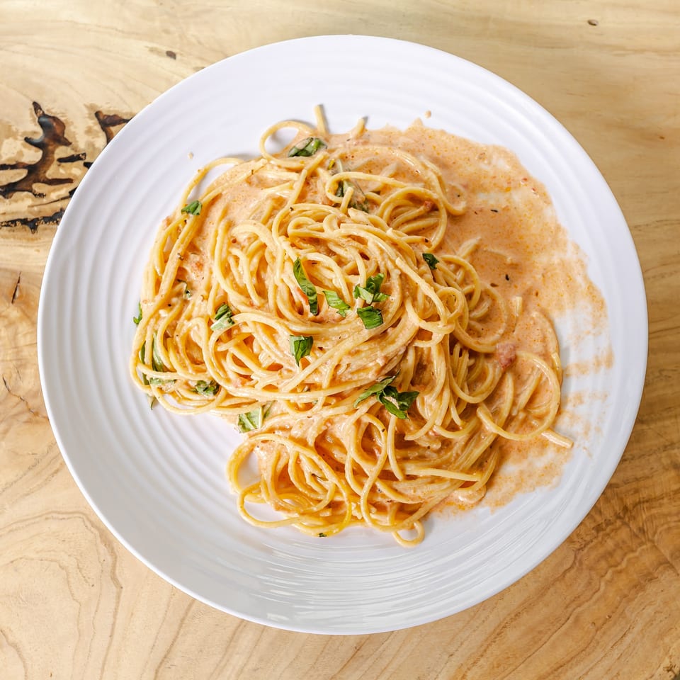 Plate of spaghetti coated in creamy tomato sauce and garnished with fresh herbs on a wooden table.