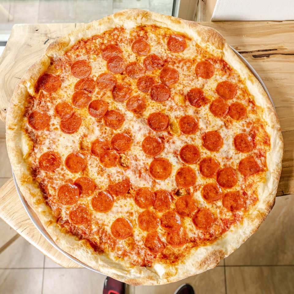 Large pepperoni pizza with melted cheese and golden crust on a wooden table.