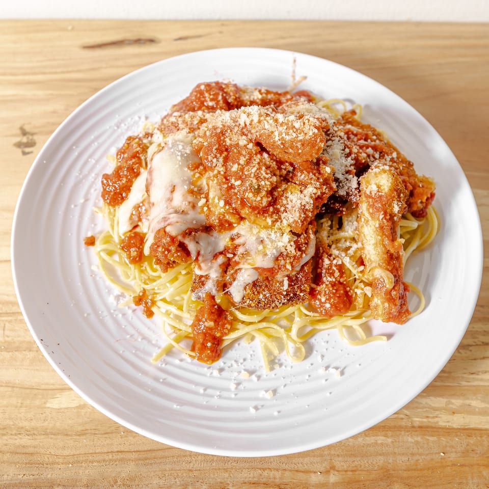 Plate of spaghetti topped with breaded chicken, tomato sauce, melted cheese, and grated Parmesan on a wooden table.